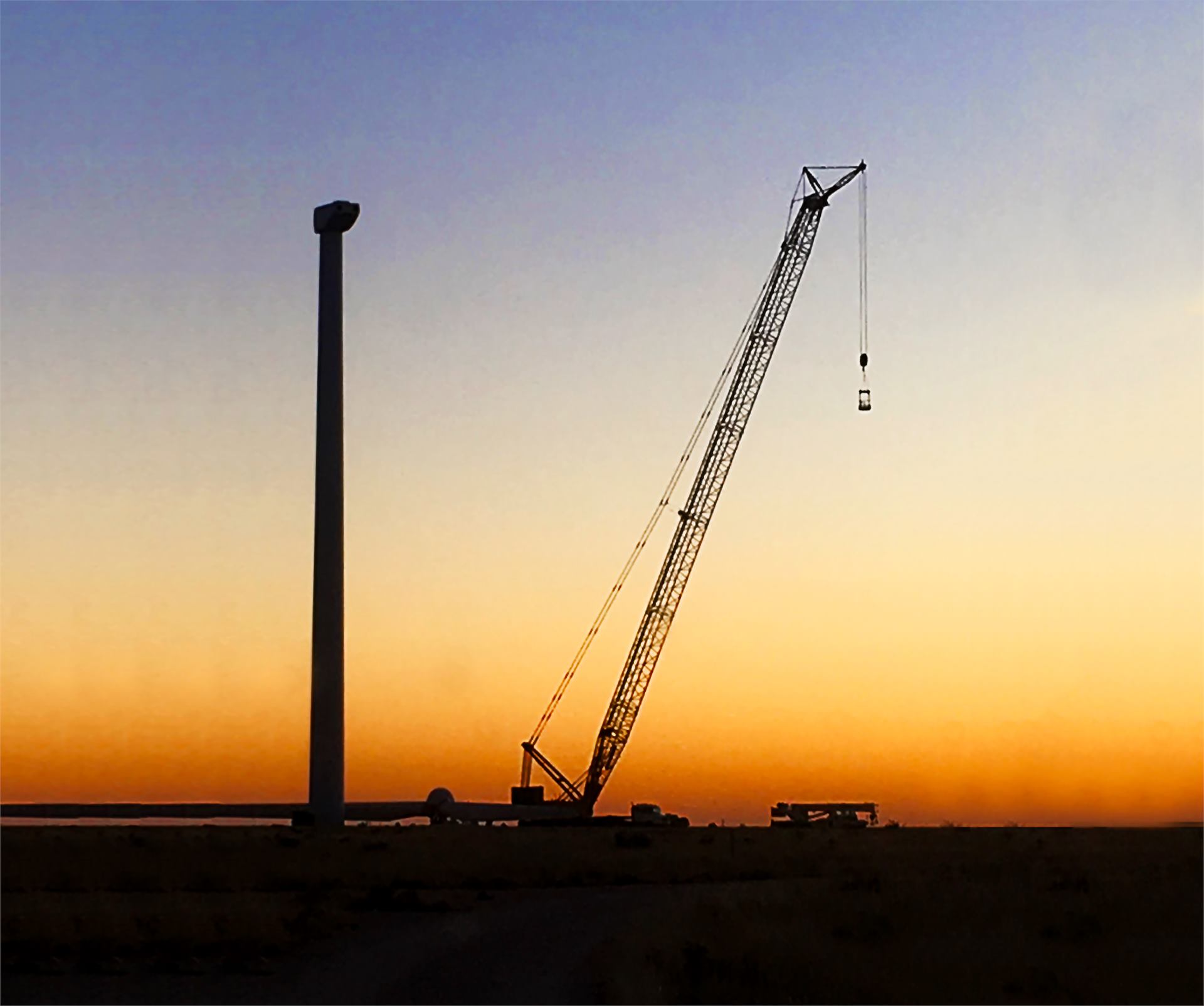 Crane silhouette at sunset beside wind tower